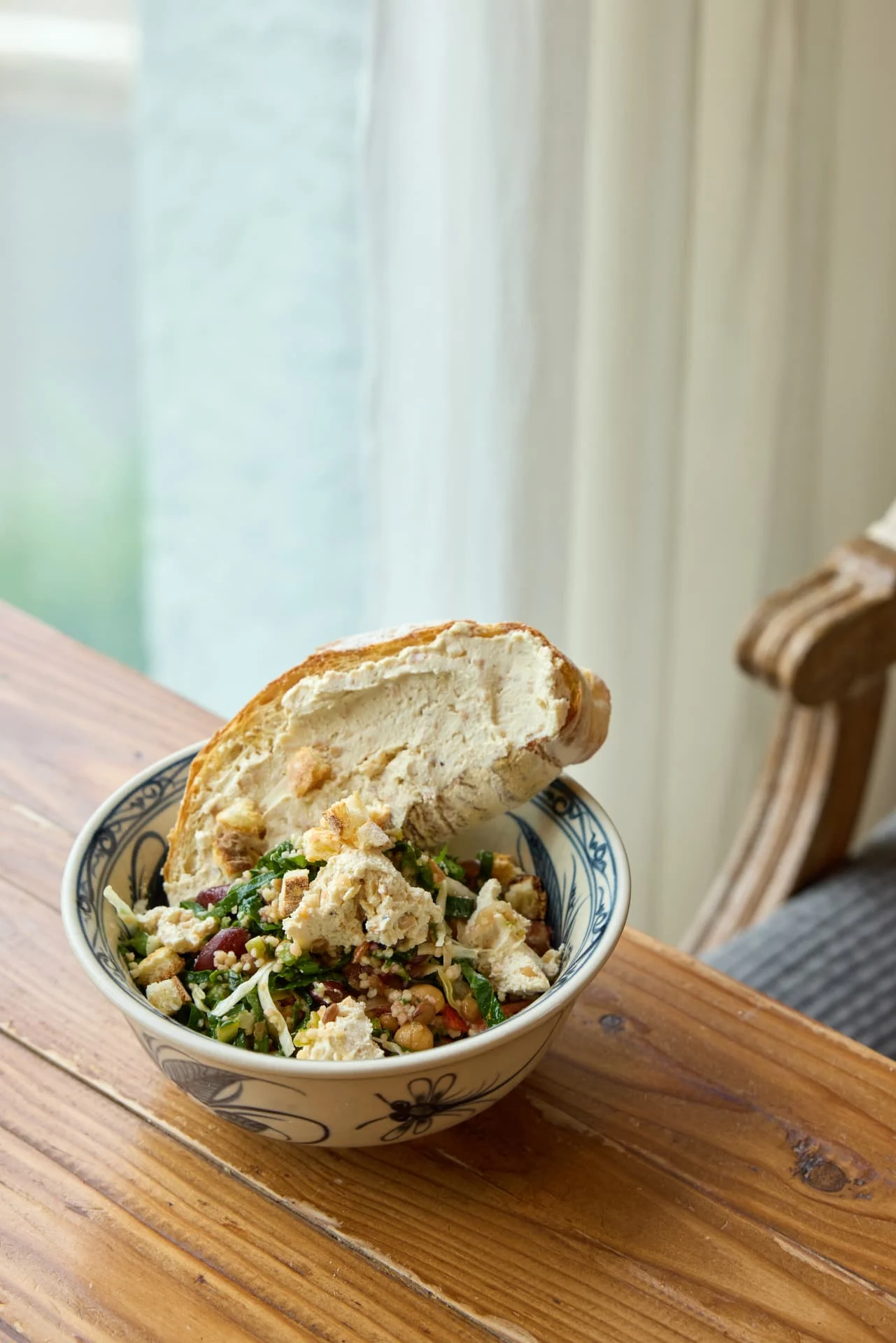 A bowl of grain salad topped with cashew cream and a slice of ciabatta