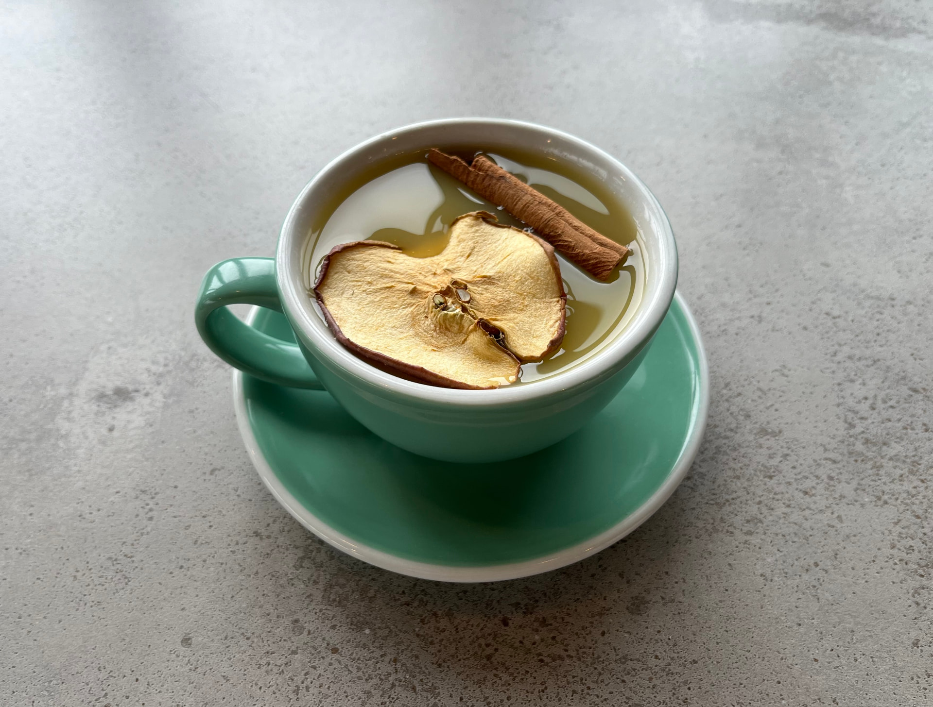 Apple ginger fruit tea with a dried apple slice and cinnamon stick in a mint-green cup