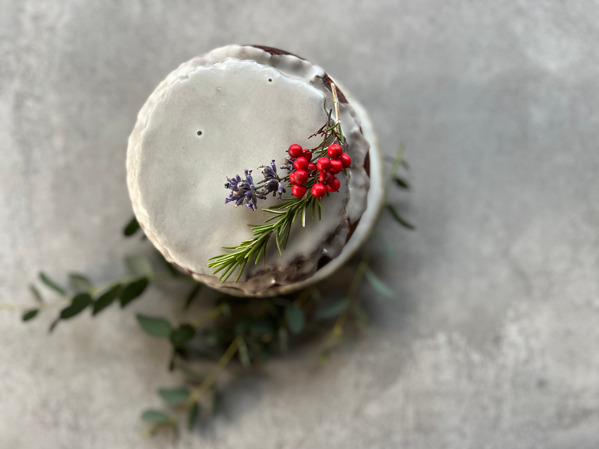 A vegan cake with icing, lavender, rosemary, and red berries