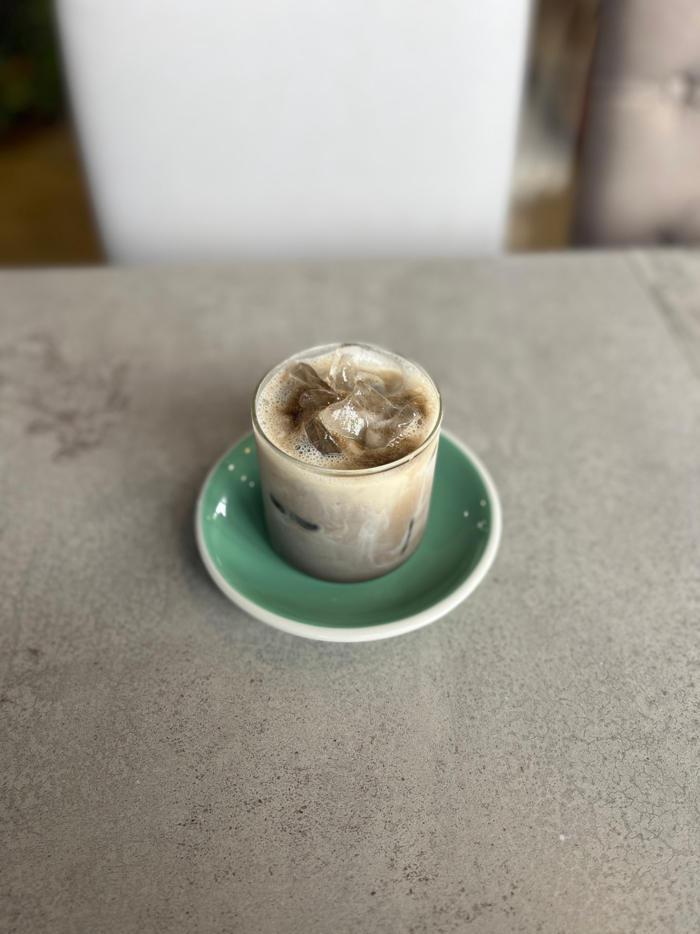 Iced hojicha matcha latte with soy milk over a mint-green saucer